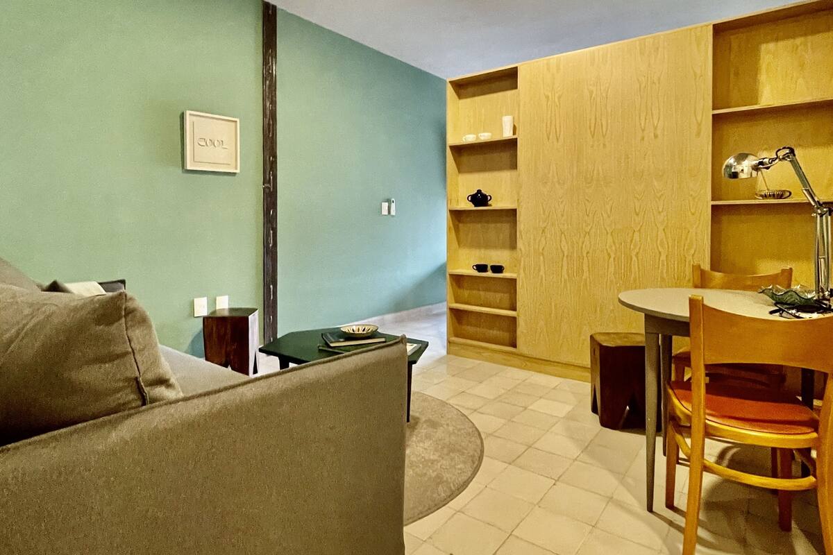 Een woonkamer met een bank, een eettafel met stoelen en ingebouwde houten planken.