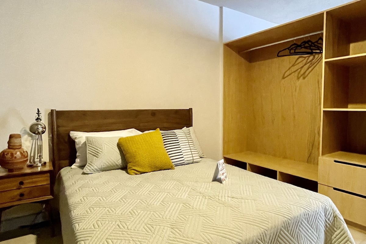 Een slaapkamer met een bed, nachtkastje, een houten kledingkast en een kledingroede.