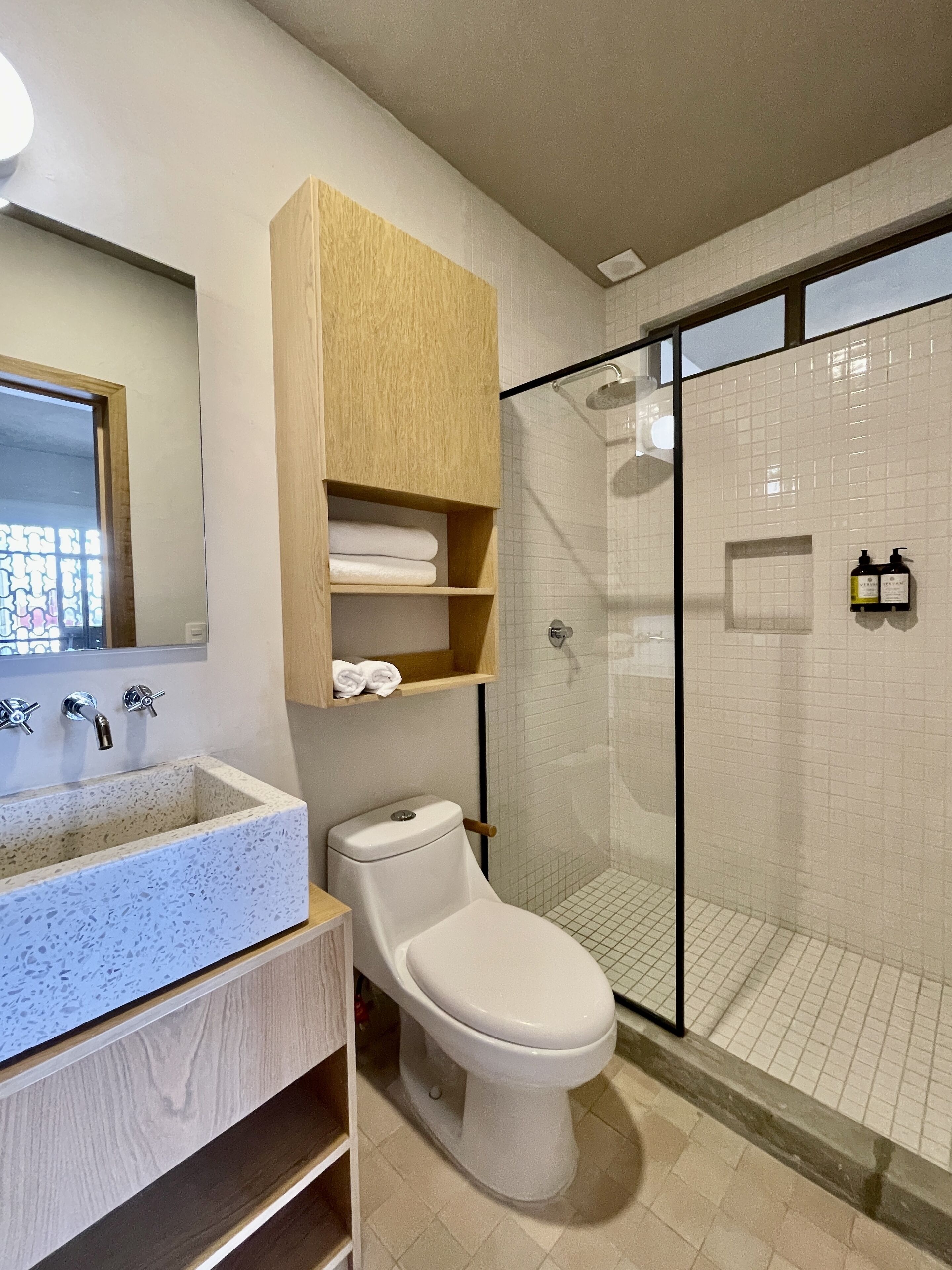 Un baño moderno con lavamanos independiente, inodoro y ducha con mampara de vidrio.