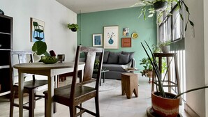 A modern living room with a dining area, featuring a sofa, a coffee table, and a dining table with chairs. There are several potted plants and artwork on the walls. - Casa San Fernando by Barrio México (Guadalajara)