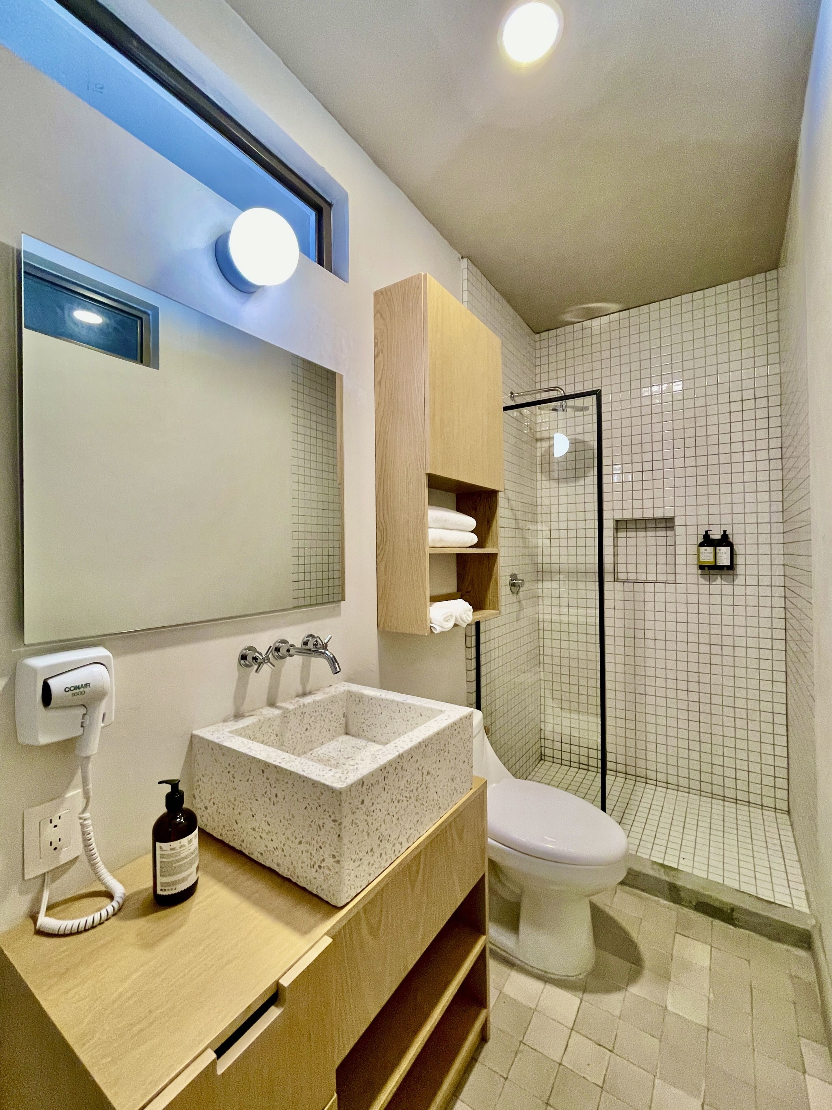 Un baño moderno con un lavamanos independiente, un inodoro, ducha con mampara de vidrio y un mueble de tocador de madera.