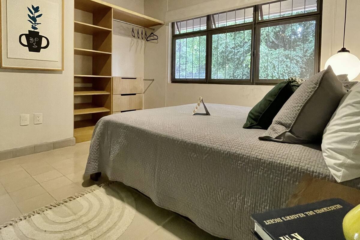 Een slaapkamer met een bed, een raam, een boekenkast en een ingelijst schilderij aan de muur.