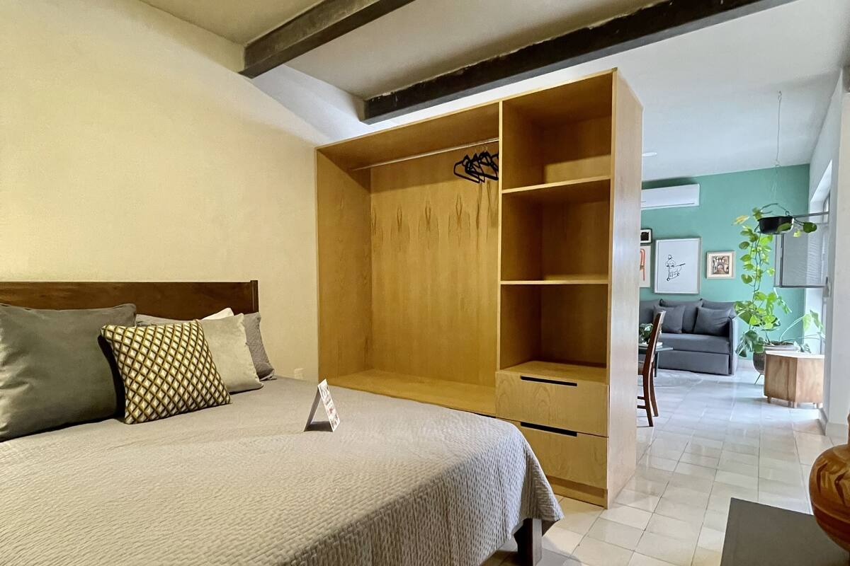 Een slaapkamer met een bed, een houten garderobe en een grijze bank op de achtergrond.