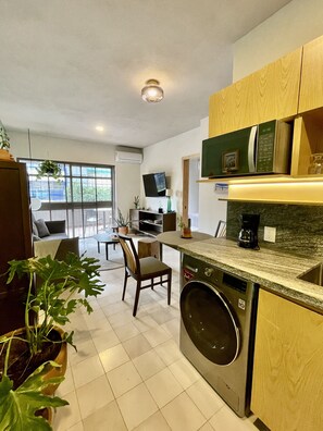 Una cocina moderna con lavadora integrada, un comedor con mesa y sillas, y un ventanal que proporciona luz natural.