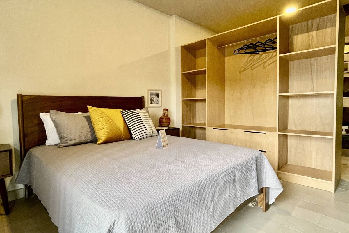 Een slaapkamer met een groot bed, een houten hoofdbord, een nachtkastje, een garderobe en een kledingrek.
