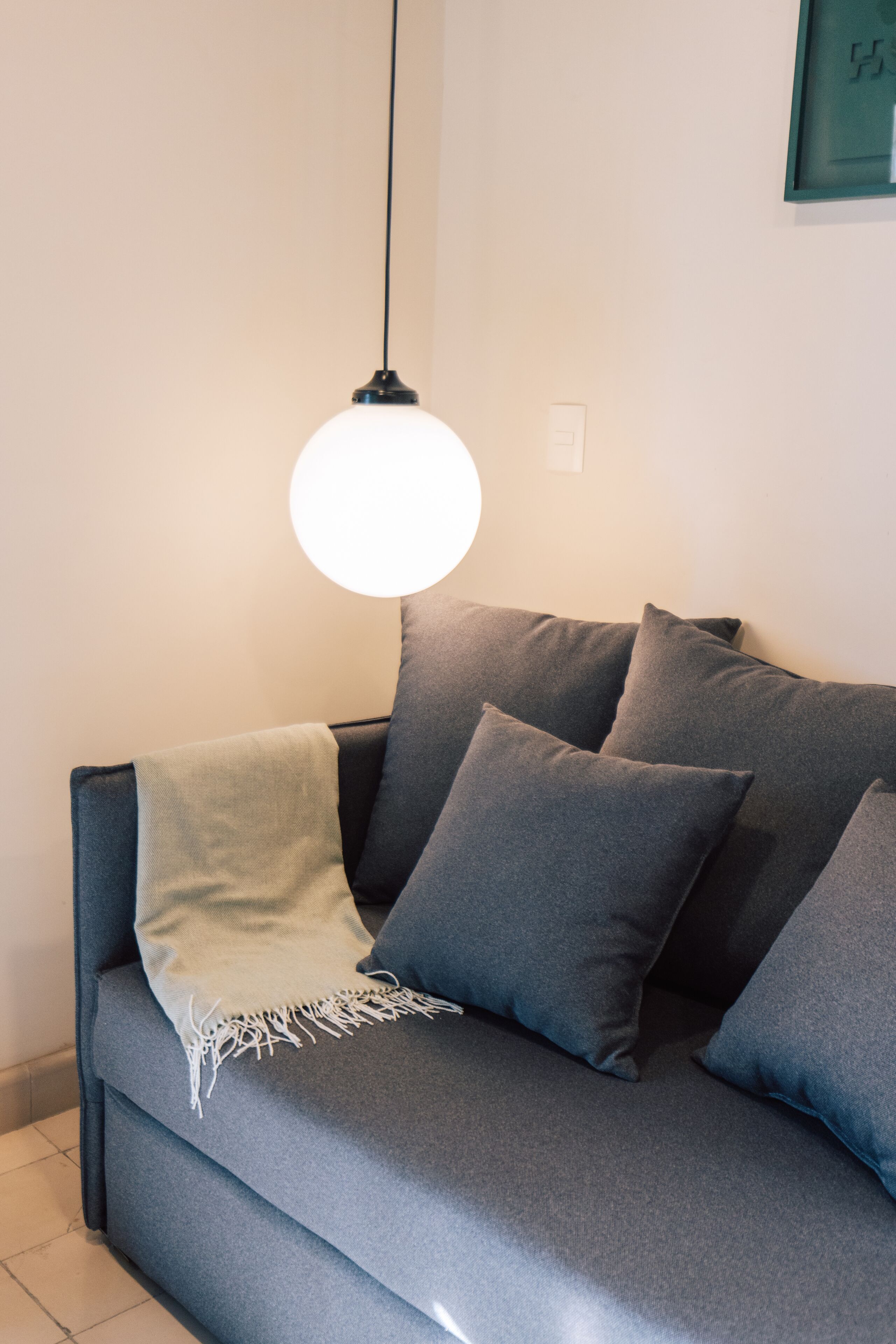 A modern living room with a grey sofa, a hanging light fixture, and a framed picture on the wall.