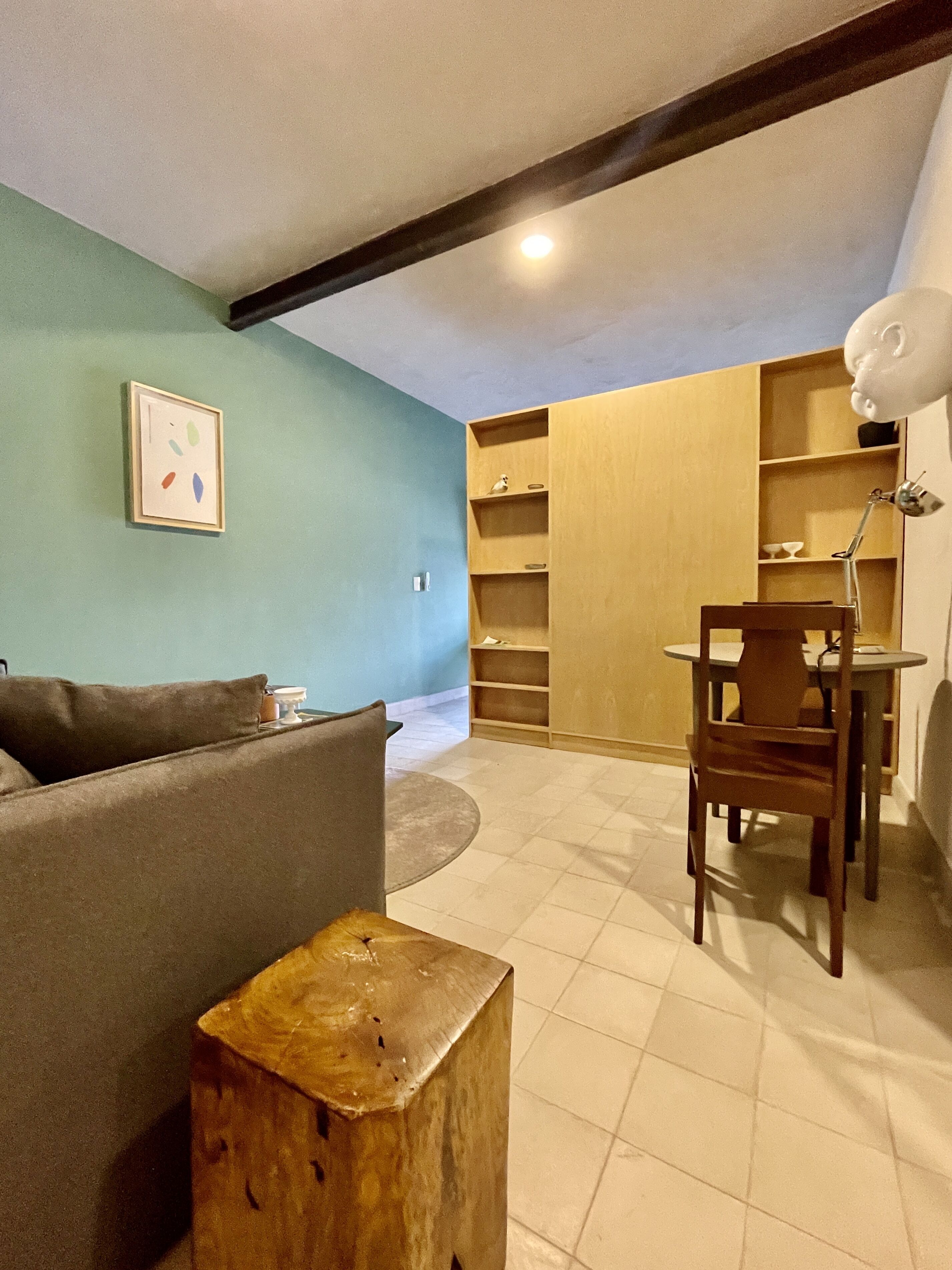 A living room with a sofa, a wooden stool, a dining table with chairs, and a bookshelf.