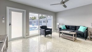 A spacious living room with a black leather sofa, a wooden coffee table, and a ceiling fan. - 2025-C Sunshine Manors (Wilton Manors)
