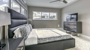 A modern bedroom with a bed, a dresser, a TV, and a ceiling fan. - 2025-C Sunshine Manors (Wilton Manors)