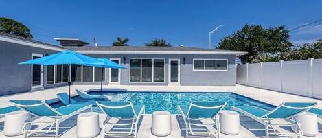 A swimming pool with lounge chairs and a blue umbrella.