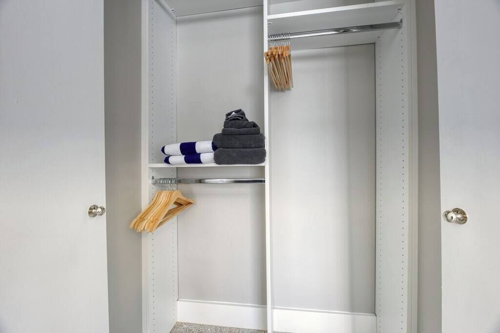 Un armario con estantes y espacio para colgar ropa, que contiene toallas dobladas, un par de zapatos y perchas de madera.
