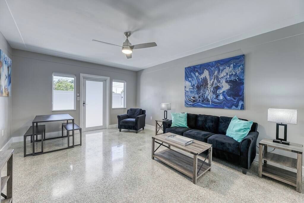 A spacious living room with a dark-colored sofa, a coffee table, a TV stand, and a ceiling fan.