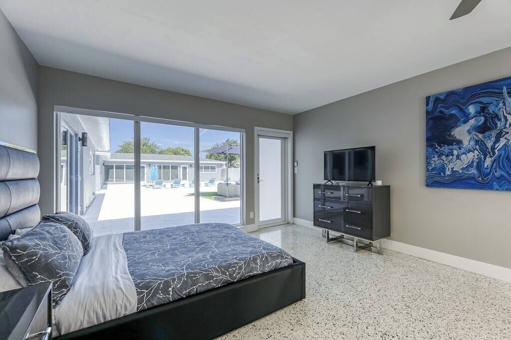 Un dormitorio moderno con una cama grande, televisión y puerta corrediza de vidrio que da a un balcón.