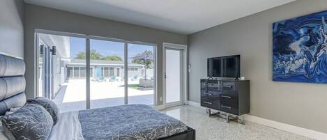 Un dormitorio moderno con una cama grande, televisión y puerta corrediza de vidrio que da a un balcón.