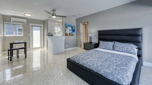 A modern bedroom with a large bed, a ceiling fan, and a view of the adjacent living area.