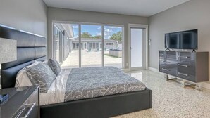 A modern bedroom with a large bed, a TV, and a sliding glass door leading to a patio.