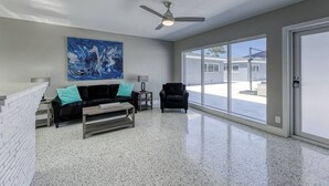 Un salon spacieux avec un canapé noir, des coussins turquoise, une table basse et un tableau accroché au mur.