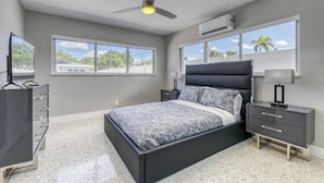 Une chambre à coucher avec un lit, des tables de chevet, un ventilateur de plafond et de grandes fenêtres.