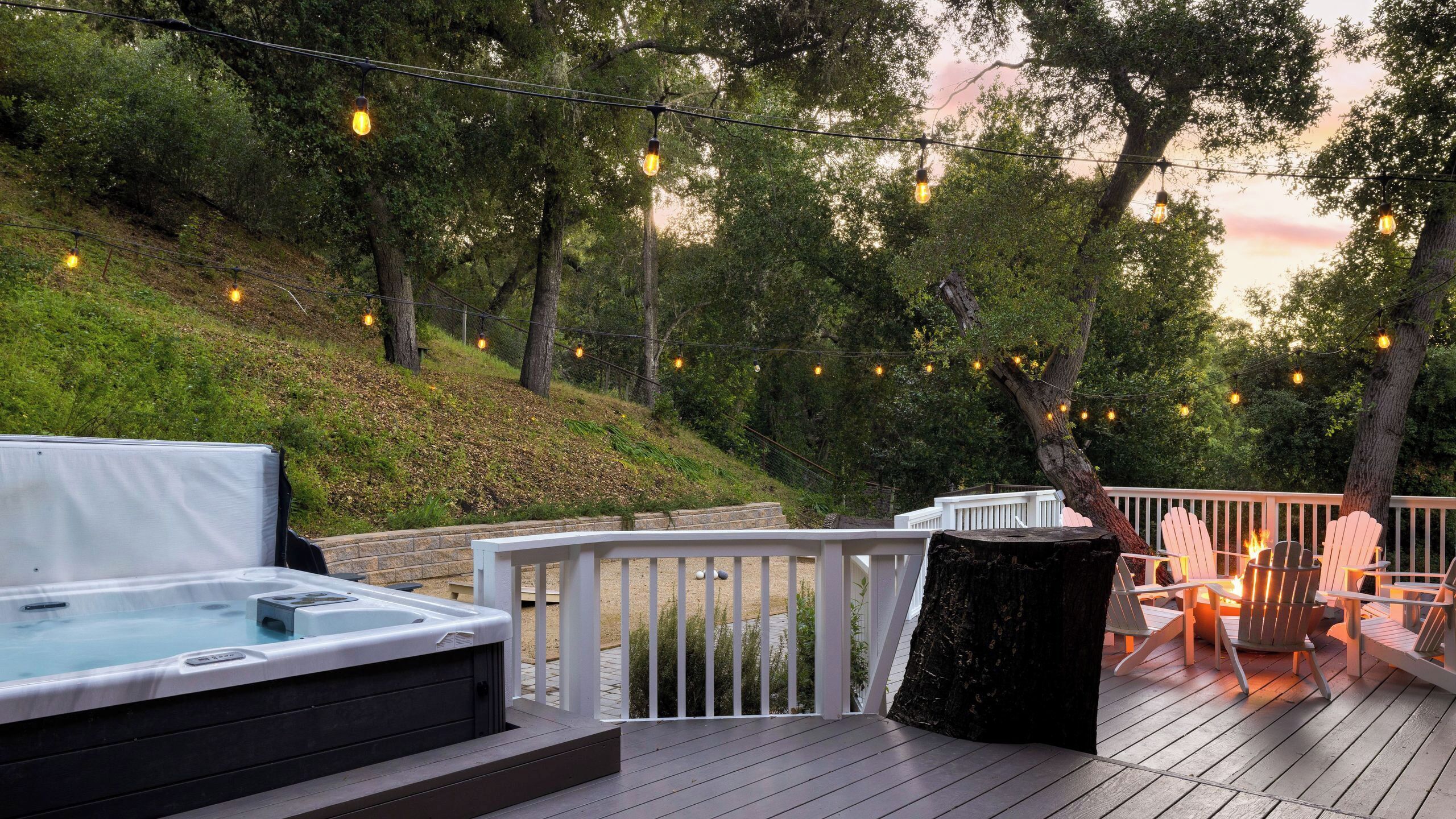 A deck with a hot tub, outdoor seating, and string lights.