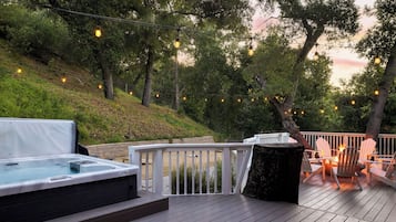 A deck with a hot tub, outdoor seating, and string lights.