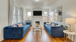 A living room with two blue sofas, a glass coffee table, a fireplace, and a mounted TV. - Heirloom by Avantstay Mins to Downtown Nashville (Nashville)