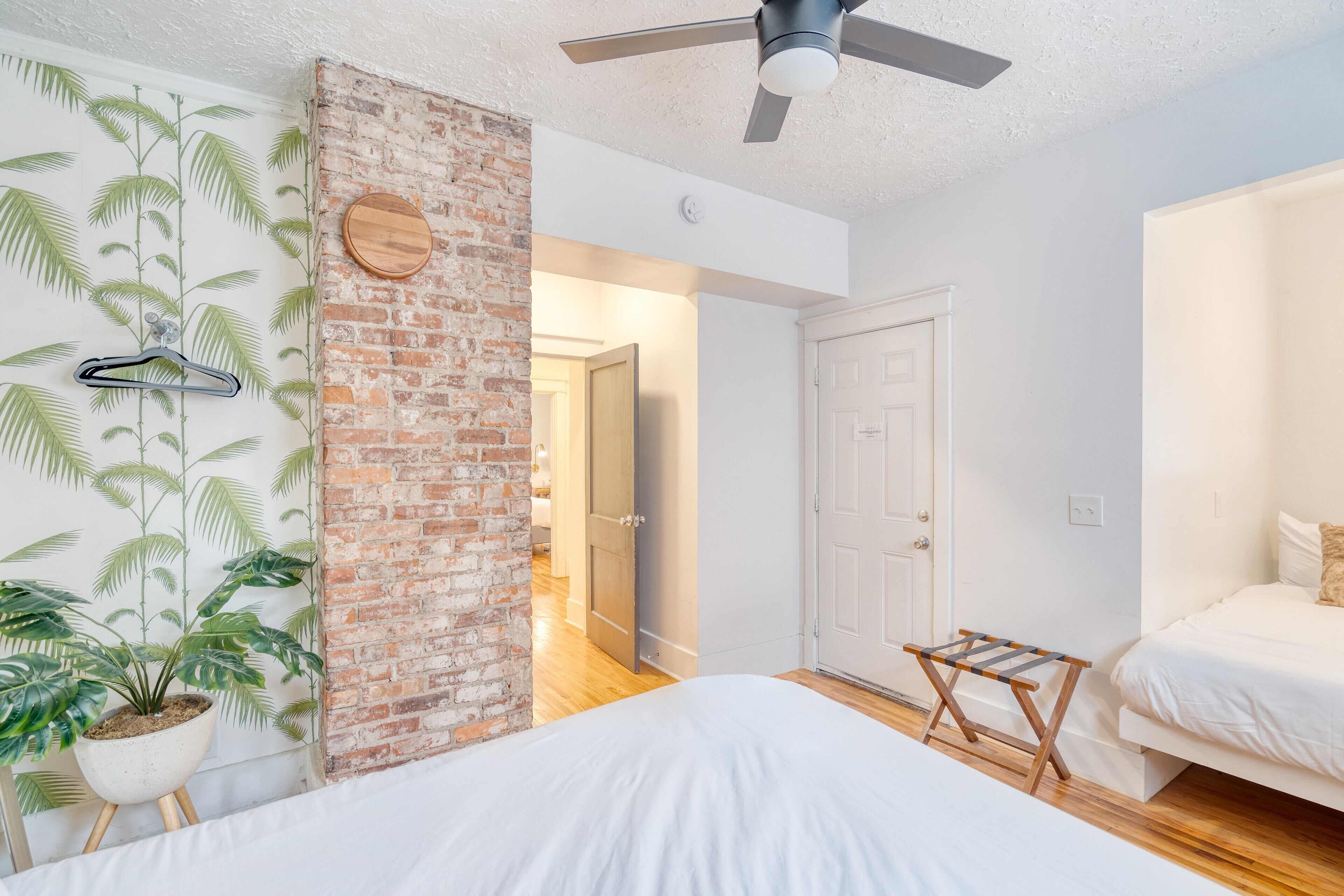 A bedroom with two beds, a brick wall, a ceiling fan, and a potted plant.