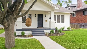 A single-story house with a front porch, a black door, and a small front yard with a tree and a hanging basket. - Heirloom by Avantstay Mins to Downtown Nashville (Nashville)