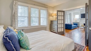 A bedroom with a large bed, a ceiling fan, and a view of a living area with a blue sofa and a kitchen in the background. - Heirloom by Avantstay Mins to Downtown Nashville (Nashville)