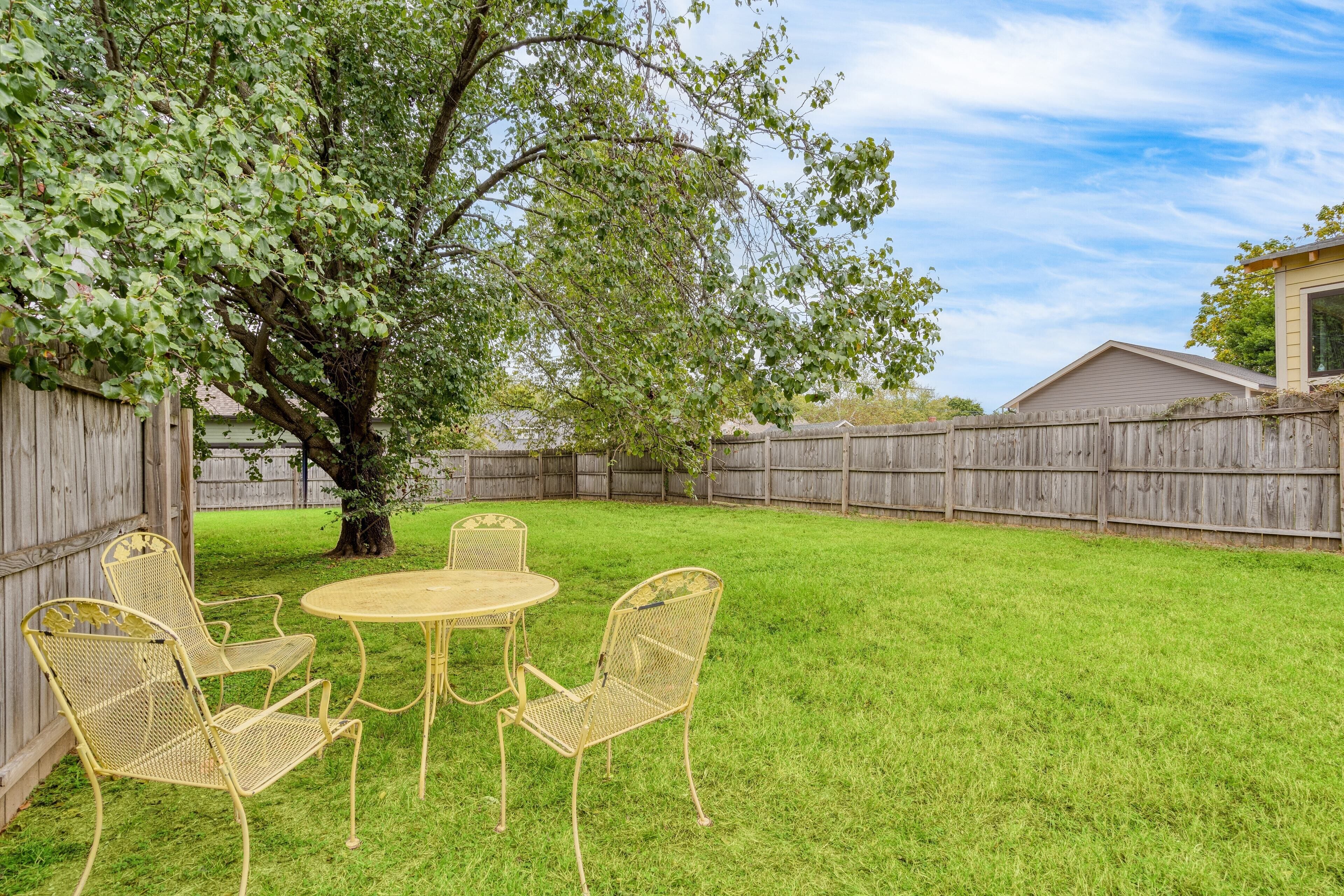 Ein Garten mit Holzzaun, Baum und Tisch mit Stühlen.