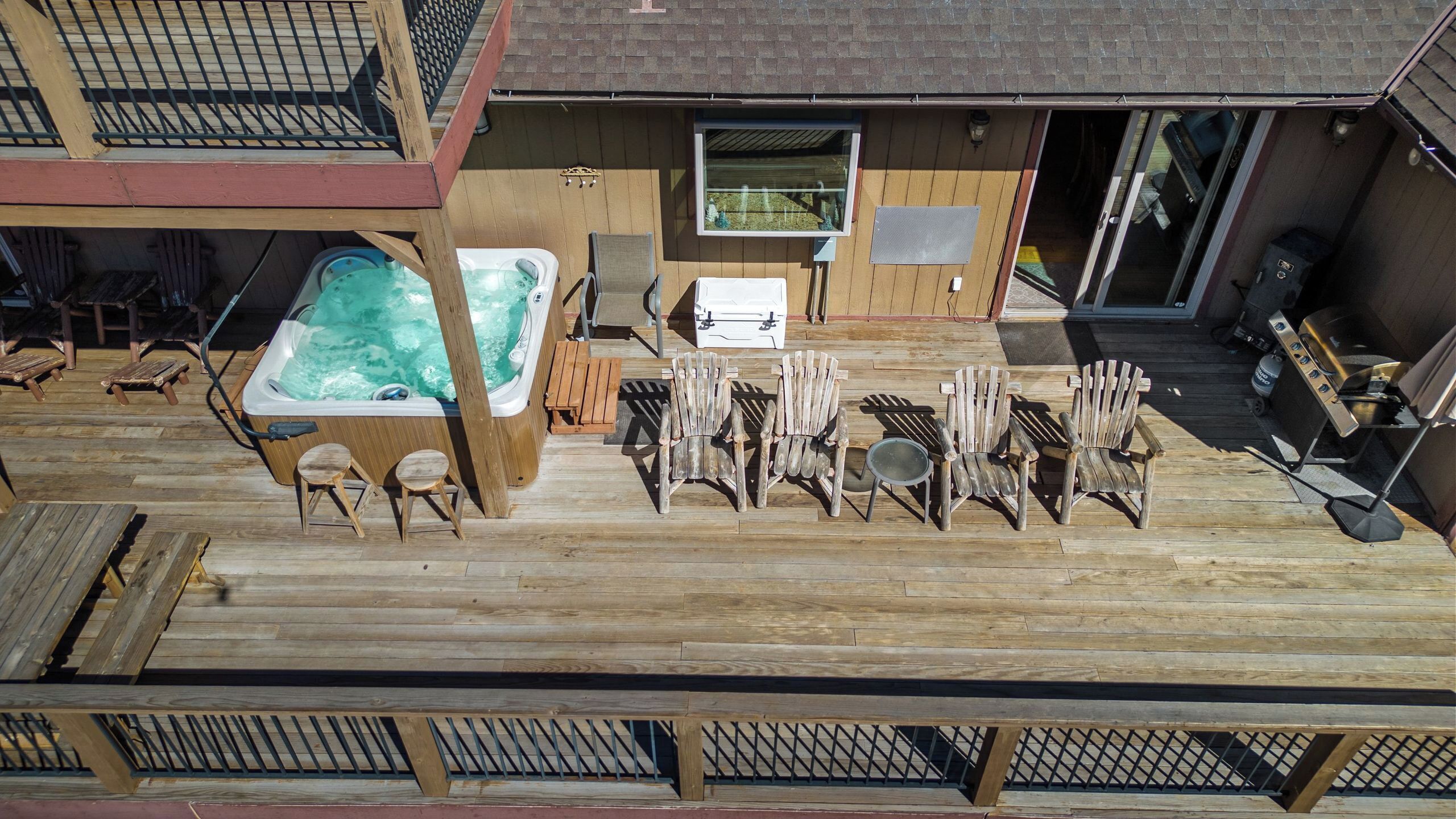 A deck with a hot tub, wooden chairs, and a barbecue grill.