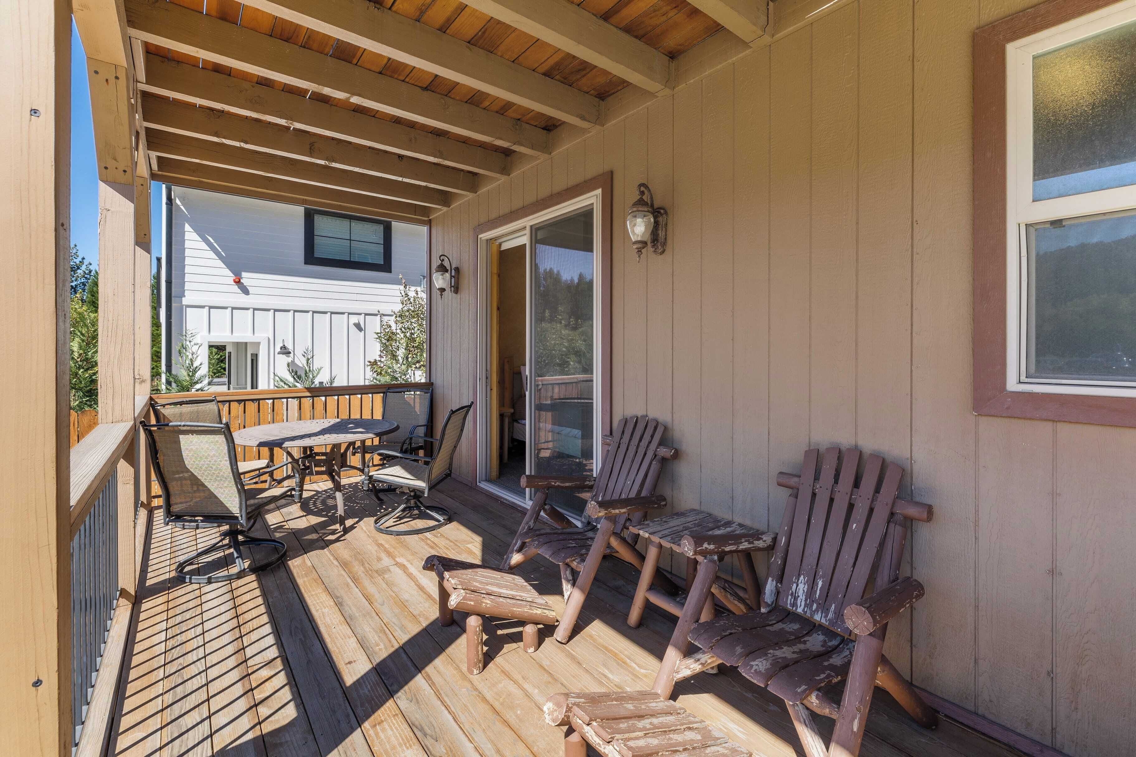 Una terrazza coperta all'aperto con mobili in legno, tra cui sedie e un tavolo, e una vista su una casa sullo sfondo.