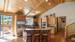 Un'ampia cucina con mobili in legno, una grande isola con sgabelli da bar, elettrodomestici in acciaio inossidabile e vista sull'esterno.