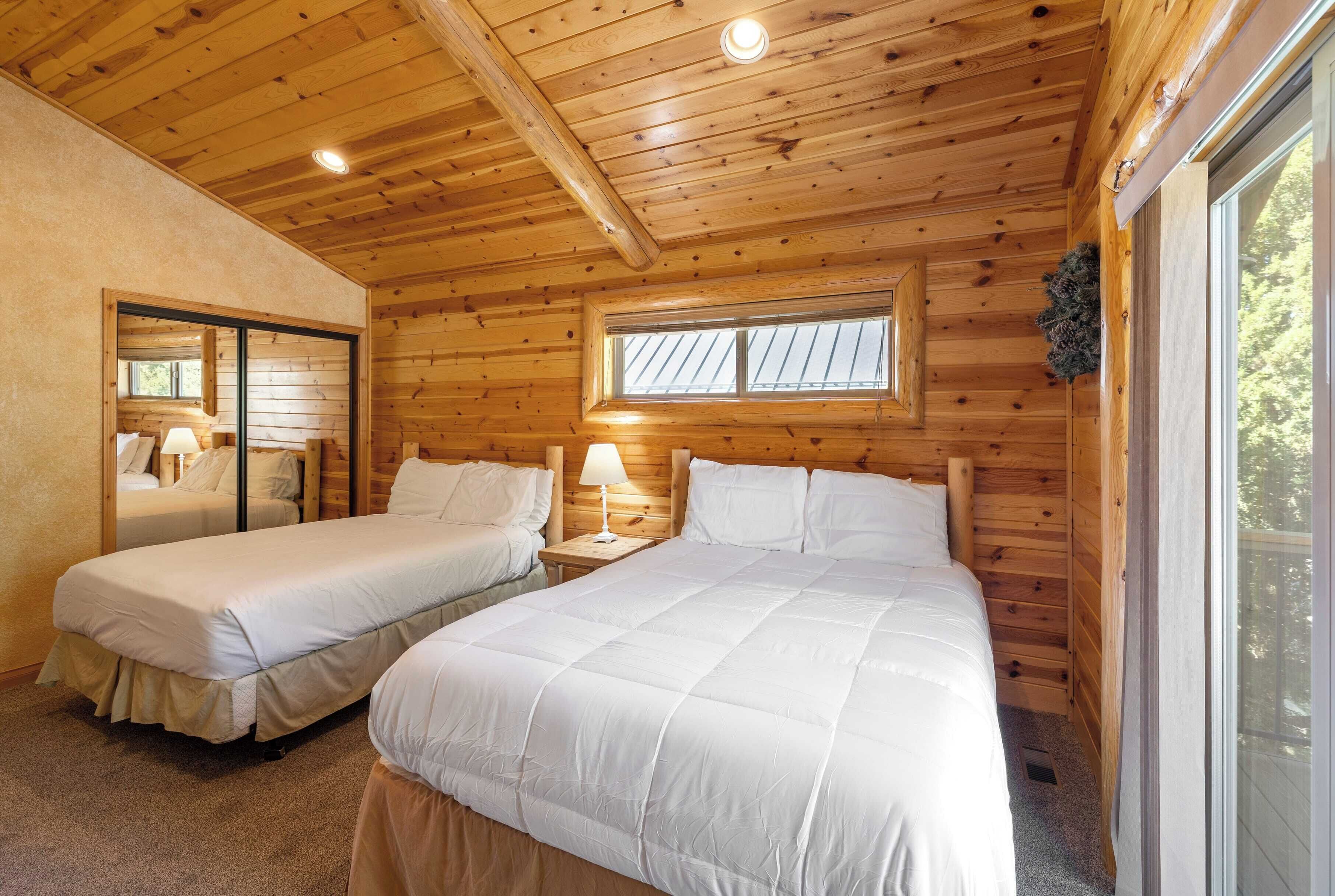 Une cabane avec deux lits, des murs en bois, une fenêtre et un luminaire au plafond.