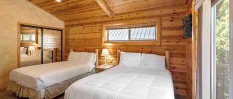 Une cabane avec deux lits, des murs en bois, une fenêtre et un luminaire au plafond.