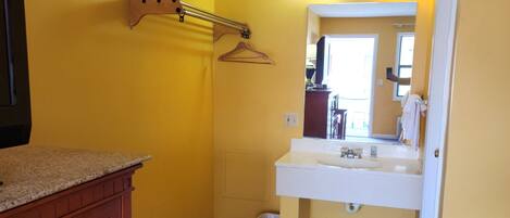 A bathroom with yellow walls, a wooden cabinet, a sink, a mirror, and a hanging towel rack.