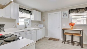 Una cocina moderna con armarios blancos, microondas, pileta y una mesa de madera con bancos.