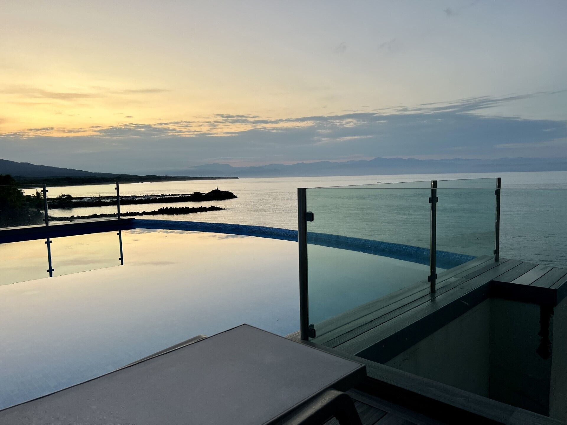 Une piscine à débordement dotée d’une balustrade en verre, offrant une vue sur une étendue d’eau paisible et des montagnes lointaines.