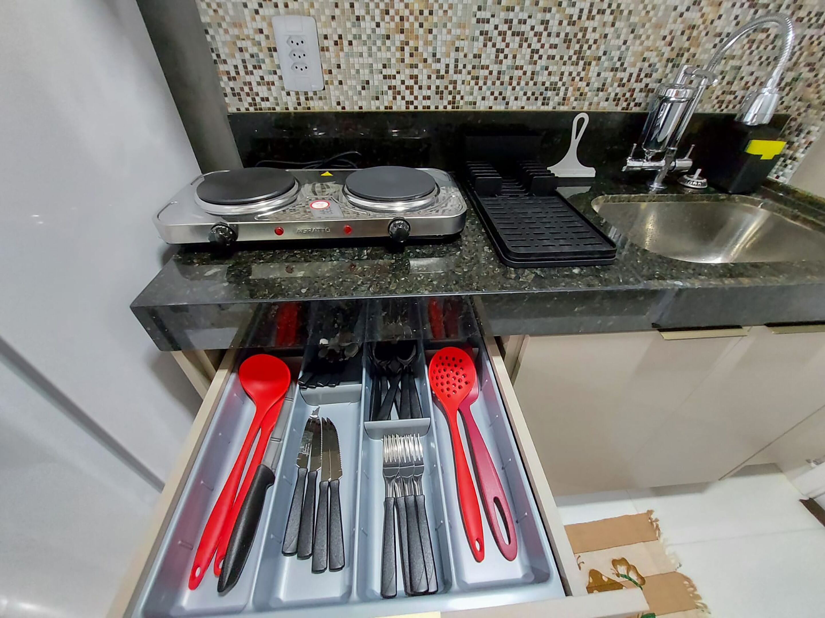 A kitchen with a gas stove, a sink, and a drawer with utensils.