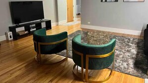 A living room with a flat-screen TV, two green upholstered chairs, a patterned rug, and abstract wall art. - Oak Park Queen (Oak Park)