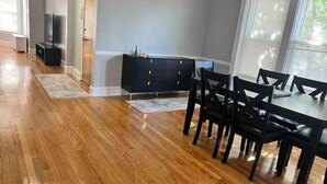 A dining area with a wooden floor, a black dining table with chairs, a dark-colored cabinet, and a television in the background. - Oak Park Queen (Oak Park)