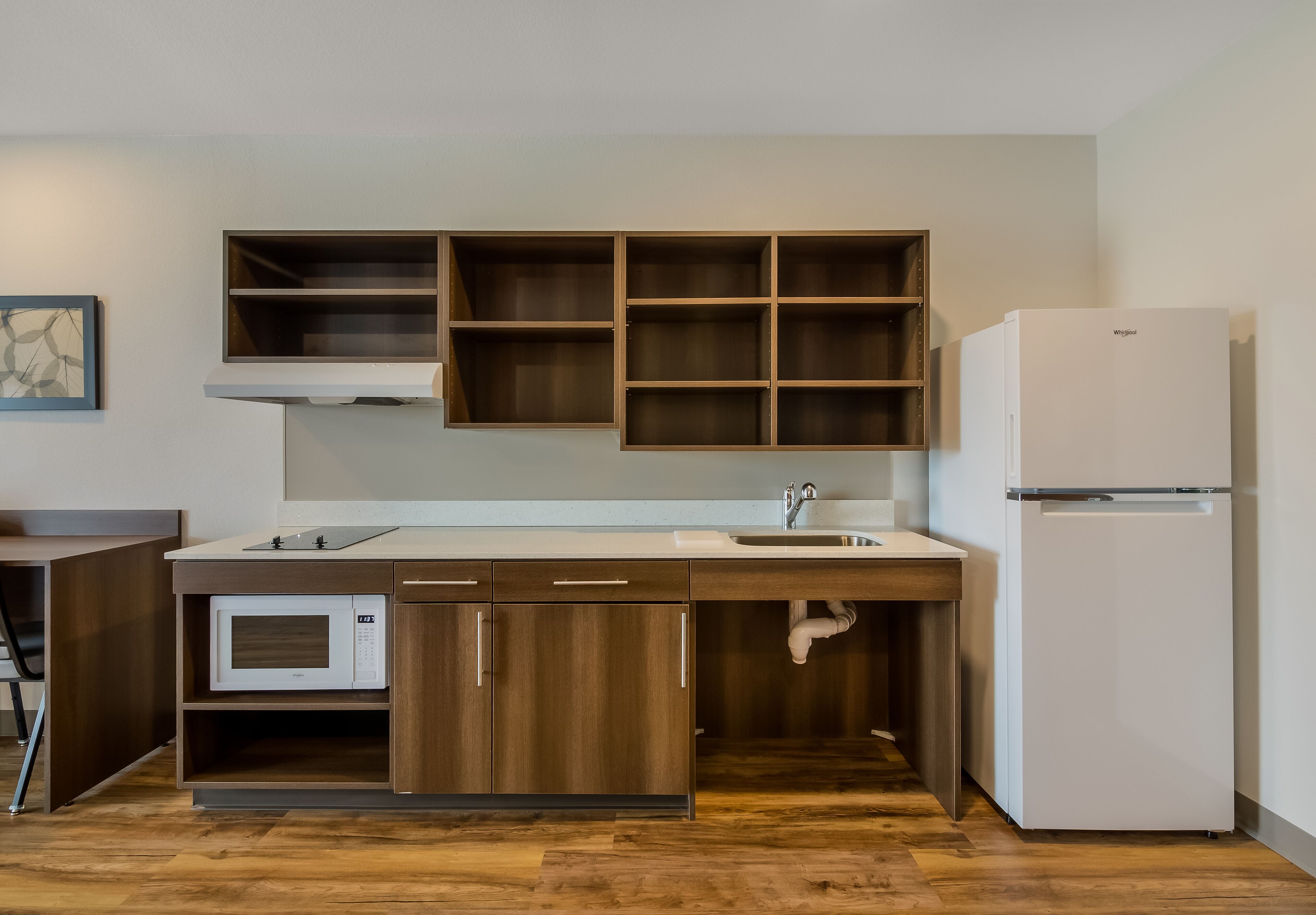 Een kleine keuken met houten kastjes, een ingebouwde magnetron, een spoelbak en een witte koelkast.
