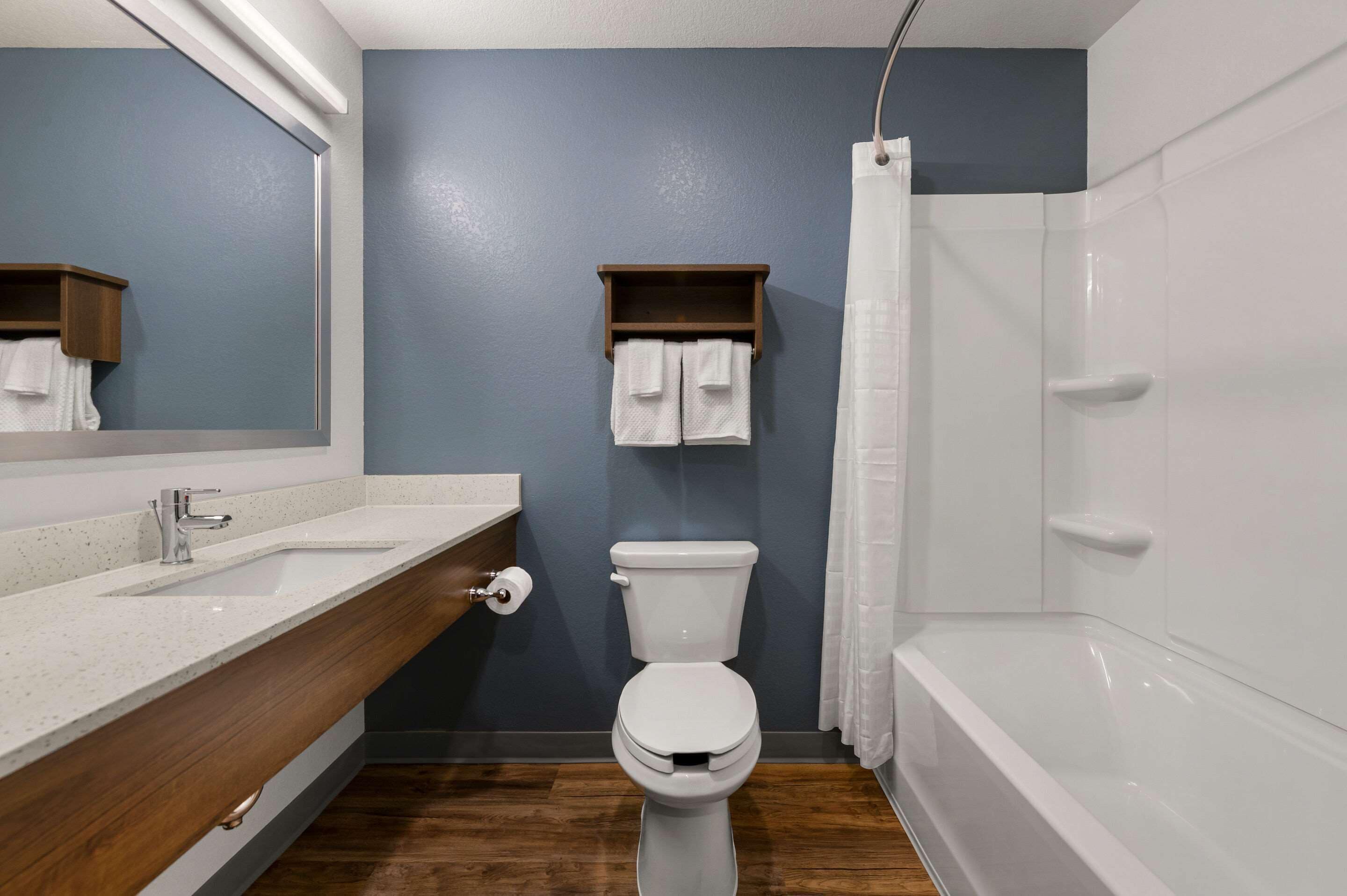 Een badkamer met een wit toilet, een wastafel met een houten kastje, een handdoekrek met twee handdoeken en een douchegordijn.