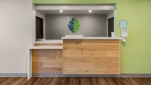 A reception desk with a green wall, a logo, and a framed certificate.