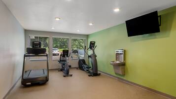 Une salle de sport équipée de tapis de course, de vélos elliptiques et d’un distributeur d’eau.