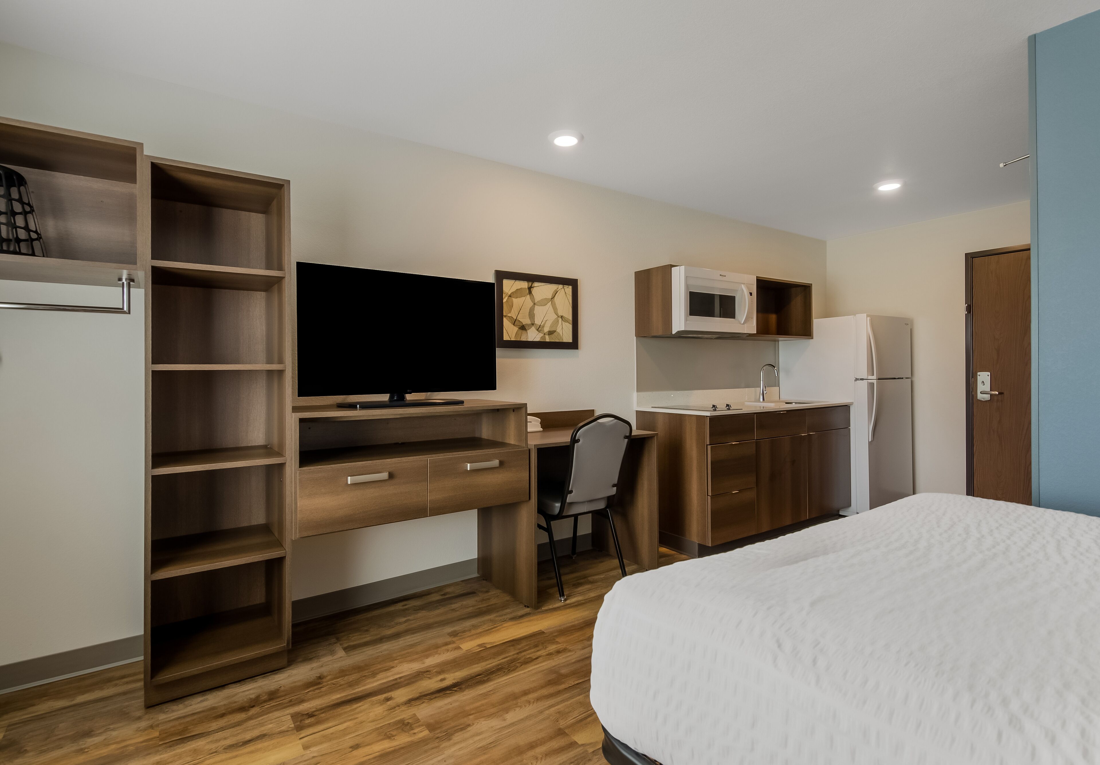 Habitación de hotel con cama, escritorio con silla, televisor, microondas, refrigerador y armario.