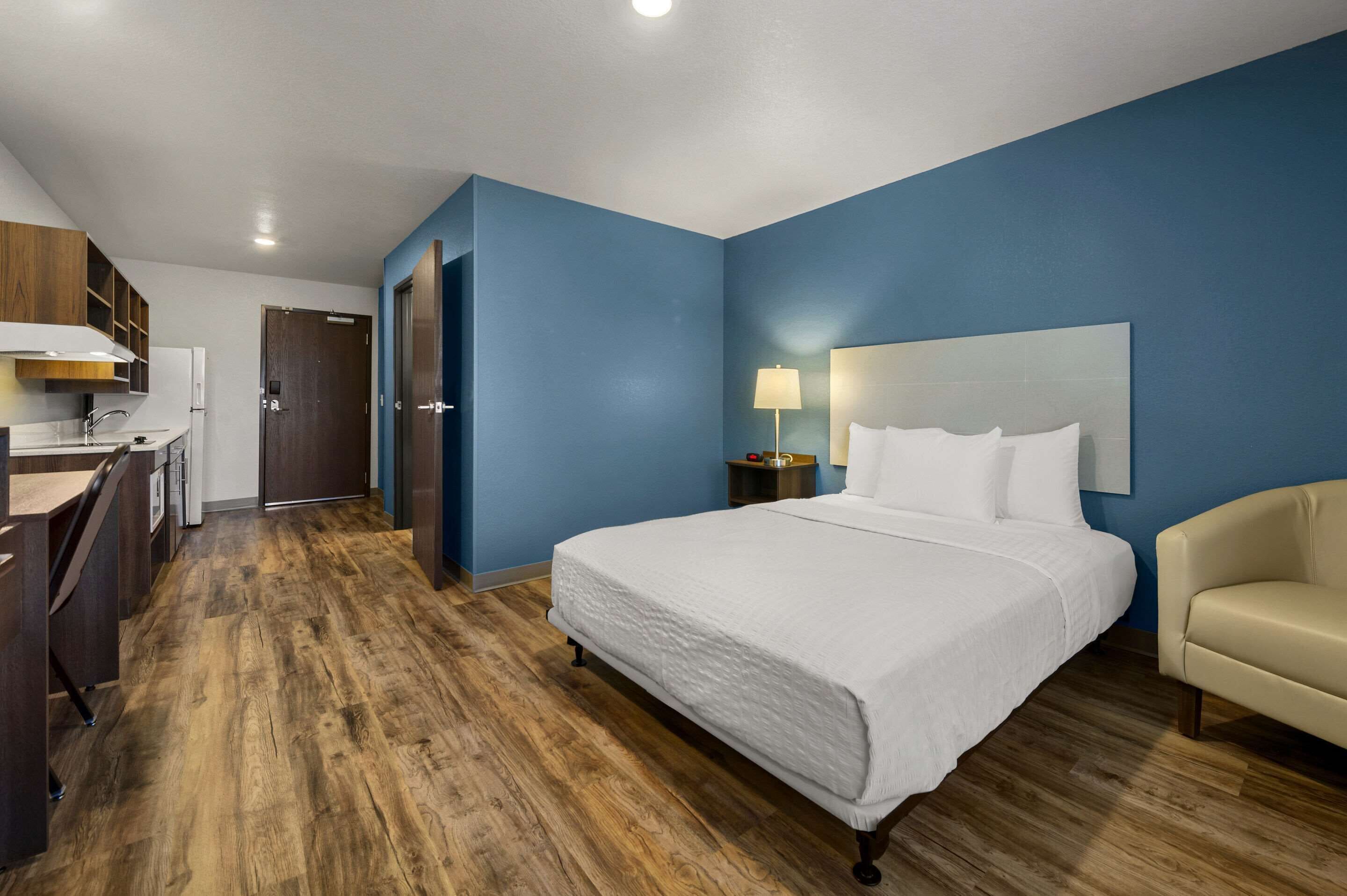 Habitación de hotel con una cama grande, un escritorio con silla, una mesita de noche con lámpara y un armario.
