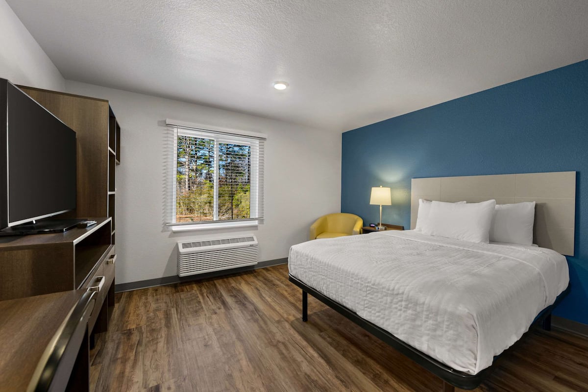 A hotel room with a large bed, a TV, a chair, and a window with blinds.
