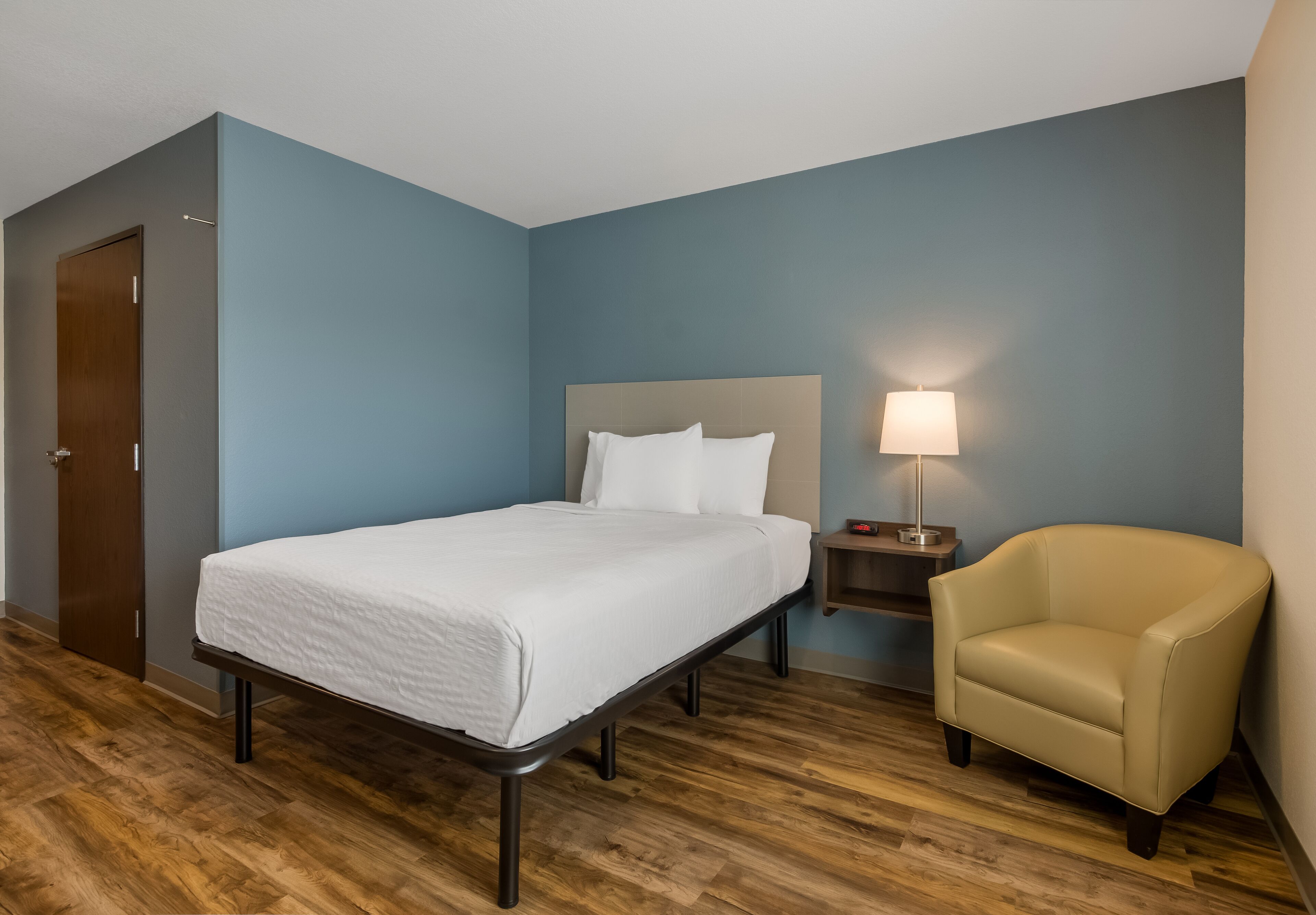 A hotel room with a bed, a chair, a nightstand, and a lamp.