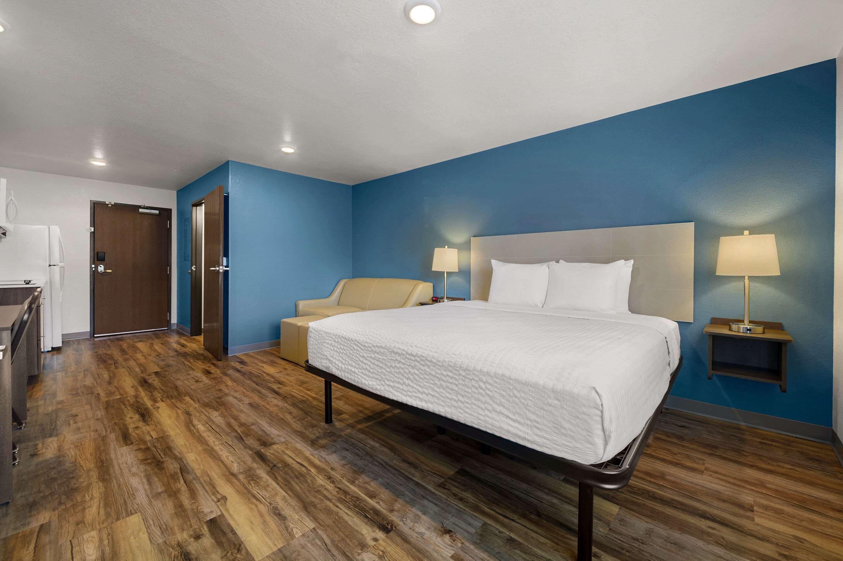 Een hotelkamer met een groot bed, twee nachtkastjes met lampen, een bank en een kitchenette.