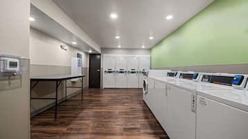A laundry room with multiple washing machines, a drying rack, and a table with a control panel.